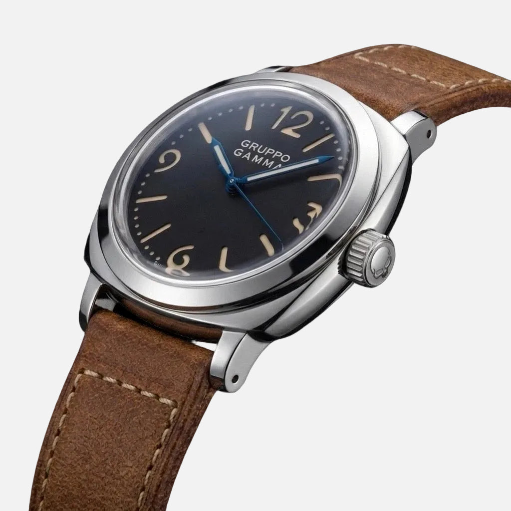 A close-up shot of a Gruppo Gamma wristwatch featuring a silver stainless steel case, a dark charcoal gray dial with beige Arabic numerals and blue hands, and a brown leather strap on a white background.