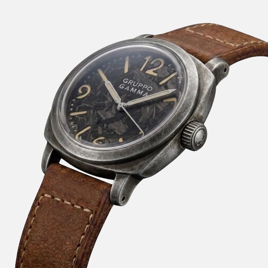A vintage-style Gruppo Gamma wristwatch with a distressed gray metal case, dark dial, and brown leather strap, shown on a plain white background.