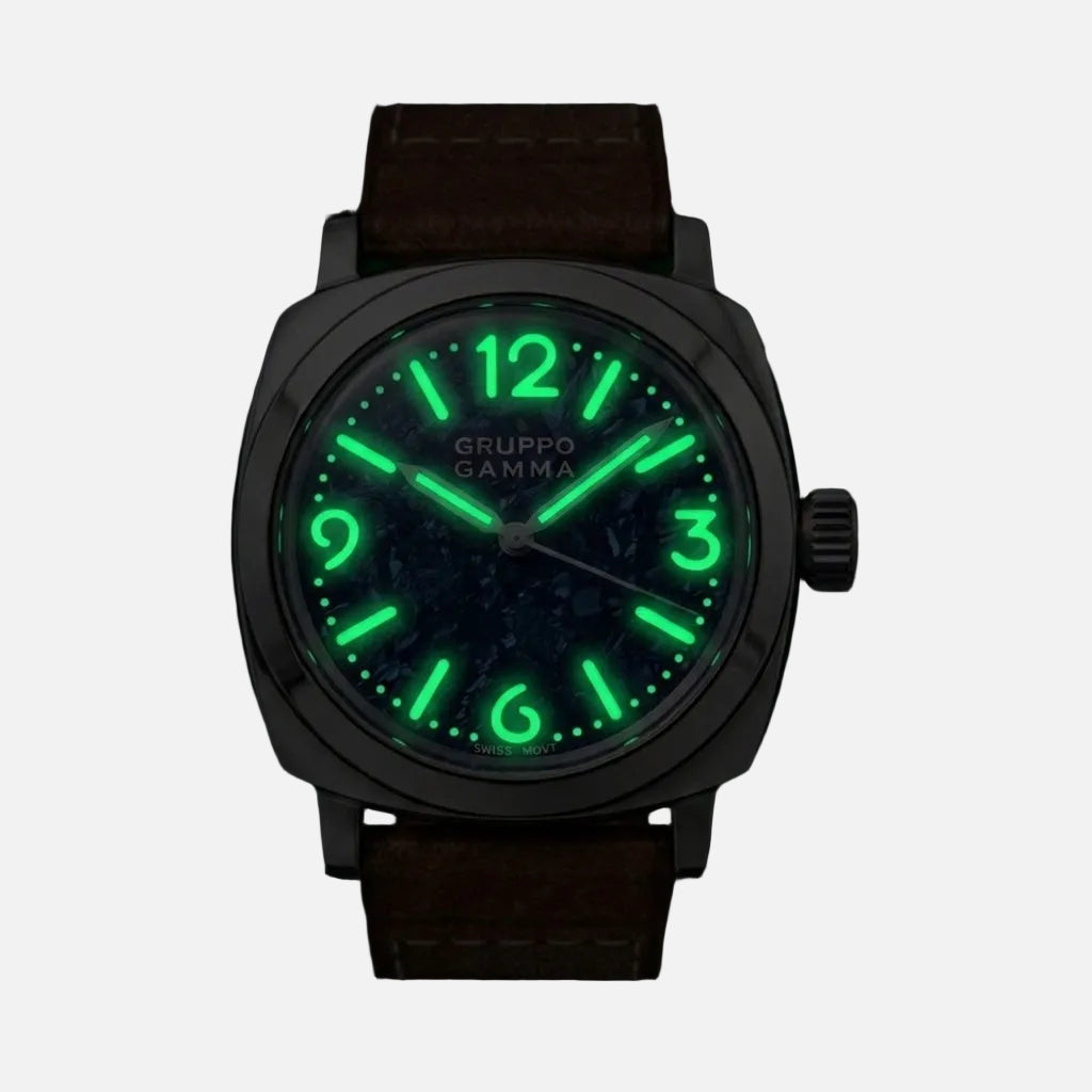 A Gruppo Gamma wristwatch with a dark brown leather strap and a dark dial featuring bright green luminescent hour markers and hands, shown against a black background.