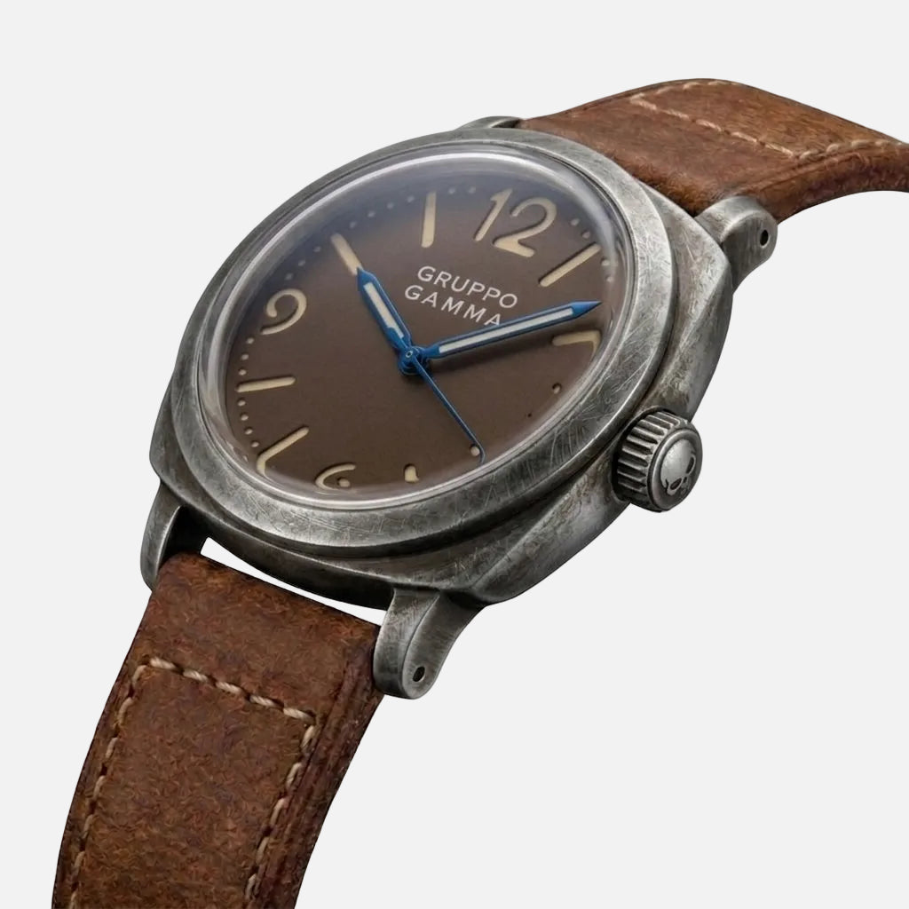A vintage-style Gruppo Gamma wristwatch with a distressed gray metal case, dark dial, and brown leather strap, shown on a plain white background.