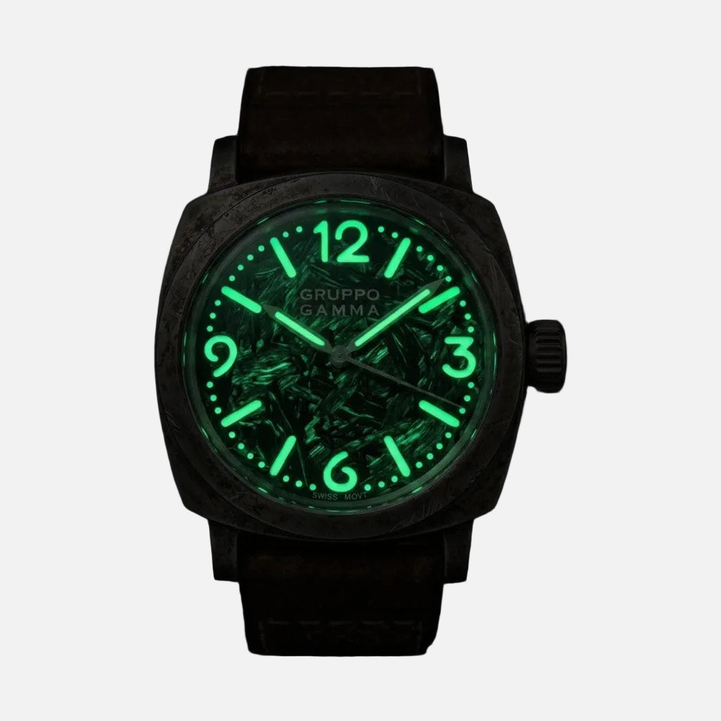 A Gruppo Gamma wristwatch with a dark textured case, a glowing green luminescent dial, and a dark brown strap, shown against a solid black background.