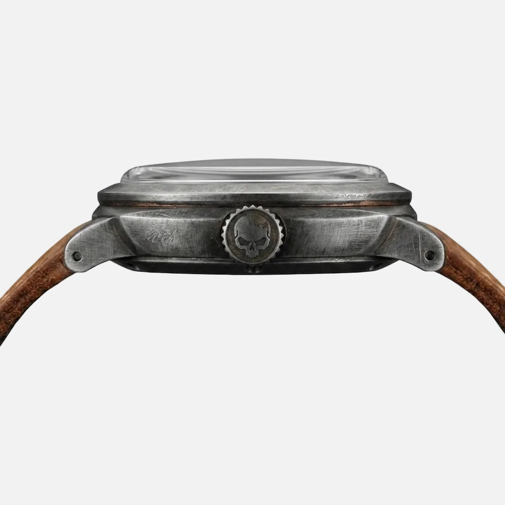 Close-up of a wristwatch case and side crown, showing a weathered silver-toned metal body with a brown leather strap on a plain white background.